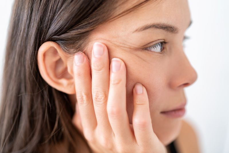 Woman with brown hair resting cheek on hand, staring into distance