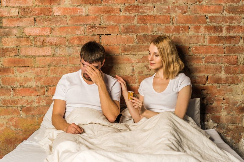 woman handing partner bottle of erectile dysfunction medication in bed