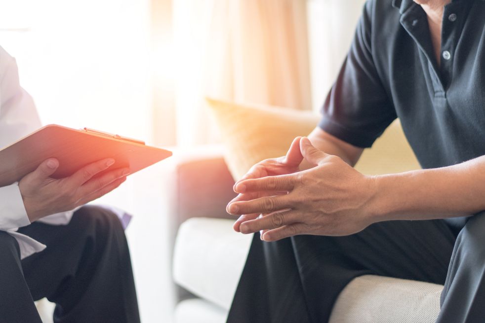 Man speaking with doctor, hands in a prayer position with elbows resting on knees