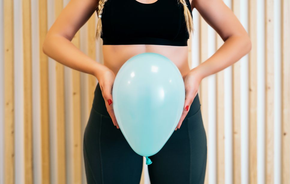 woman in black workout gear holding light blue balloon in front of pelvis
