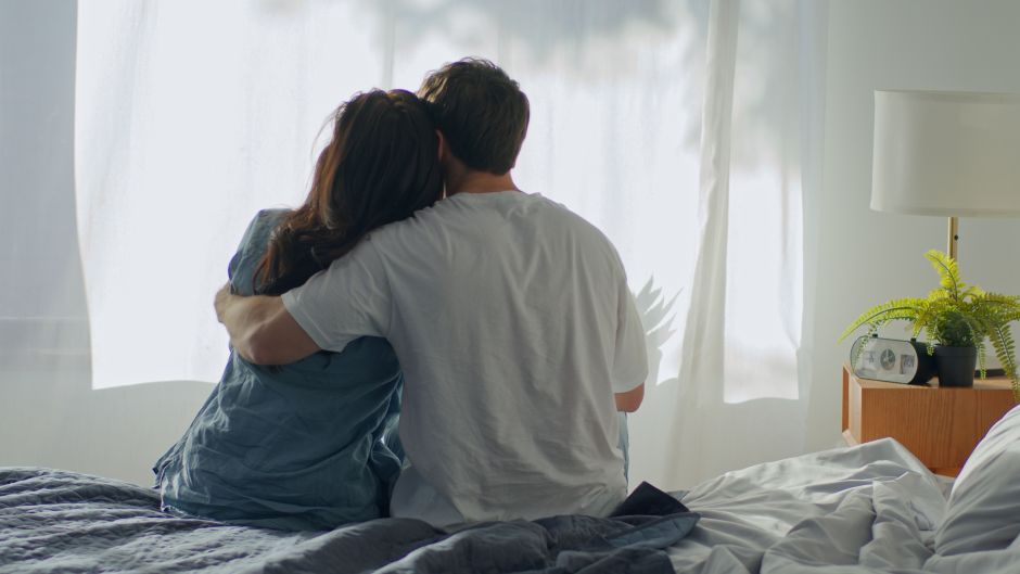 couple sitting on the edge of the bed in a side hug